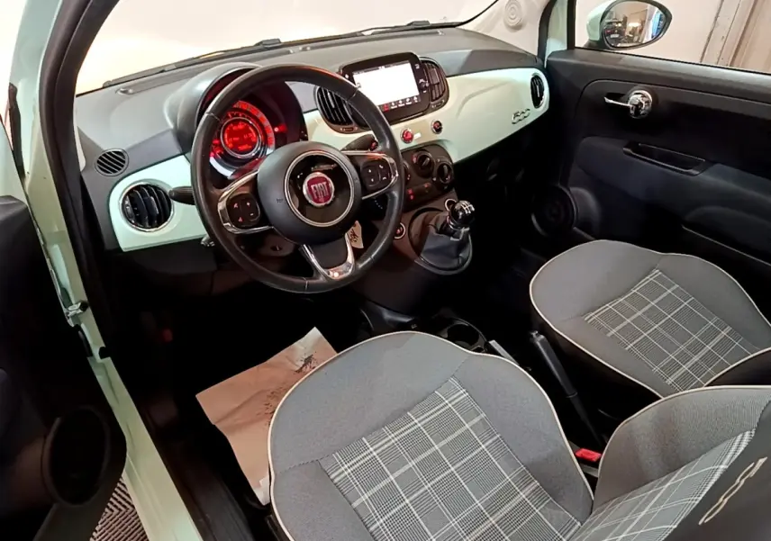 Vue intérieure côté conducteur de la FIAT 500 verte, tableau de bord clair et sièges gris à motifs carreaux.