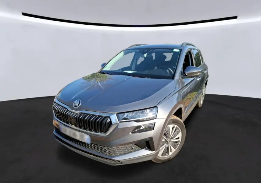 Vue 3/4 avant d'un Skoda Karoq gris métallisé avec calandre chromée et jantes alu 17 pouces sur fond neutre.