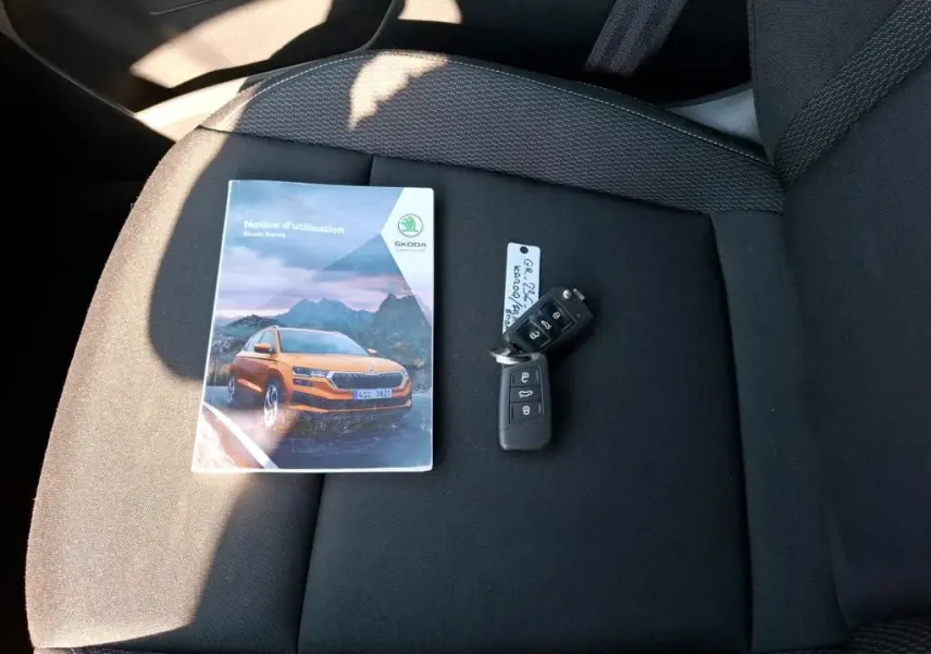 Vue rapprochée sur siège noir avec notice Skoda Karoq orange et clé de voiture noire posées dessus.