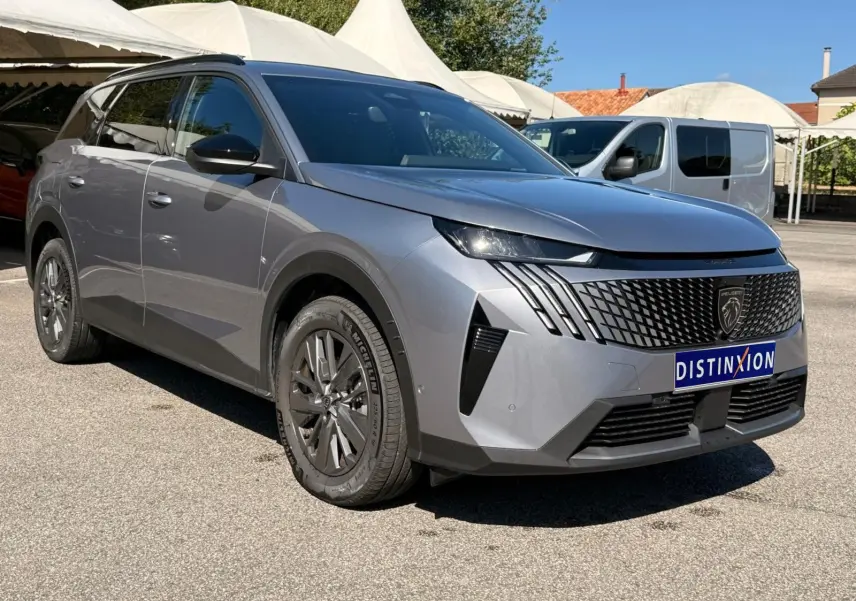 Peugeot 5008 gris Artense en 3/4 avant droit, avec calandre noire distinctive et jantes foncées sous un ciel dégagé.