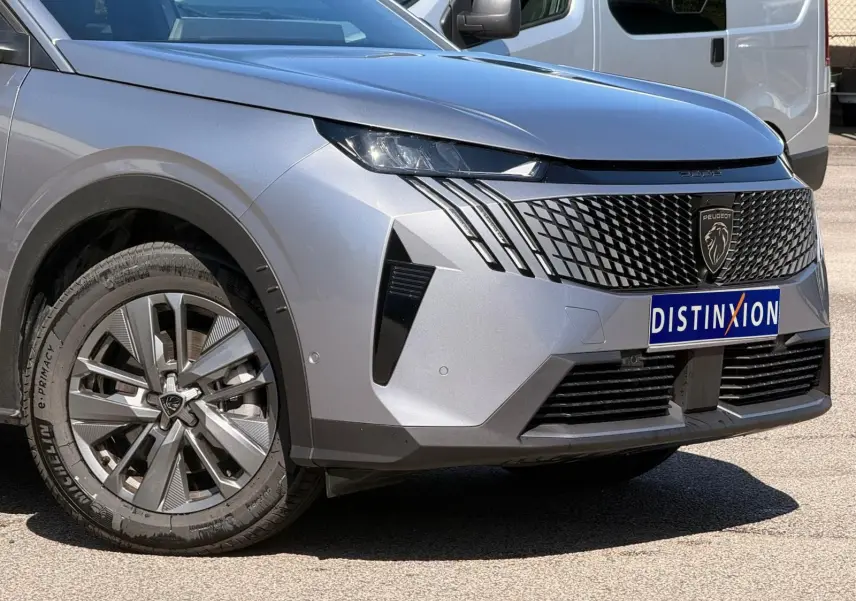 Vue 3/4 avant gauche du Peugeot 5008 2025 gris Artense avec calandre noire et phares LED distinctifs.