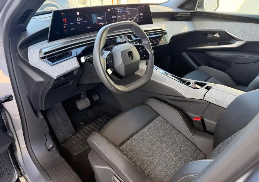 Vue intérieure côté conducteur du Peugeot 5008 1.2 Hybrid 145 Allure 2025, avec tableau de bord numérique et sellerie gris clair et noir.