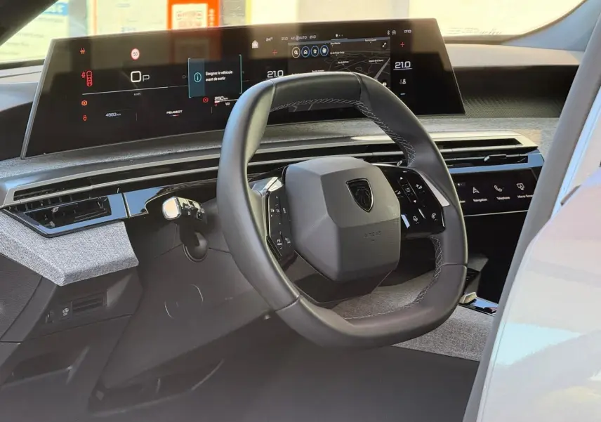 Vue intérieure du tableau de bord et volant du Peugeot 5008 gris Artense, avec écran numérique panoramique et commandes tactiles intégrées.