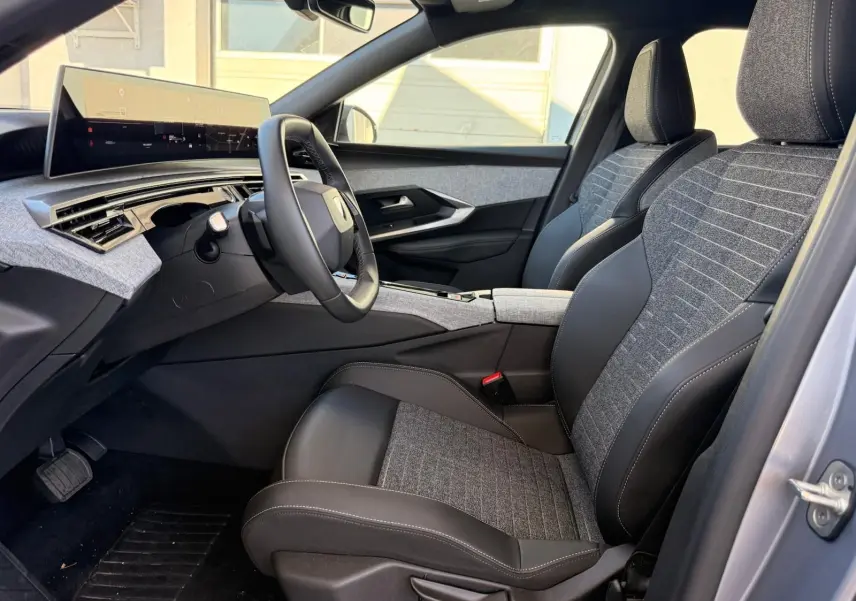 Vue intérieure côté conducteur du Peugeot 5008 1.2 Hybrid 145 Allure 2025, sièges tissu gris et cuir noir, tableau de bord moderne.
