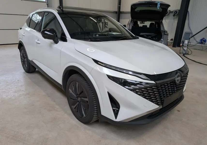 Nissan Qashqai blanc nacré vu en 3/4 avant droit, avec calandre noire et jantes alliage foncé dans un garage.