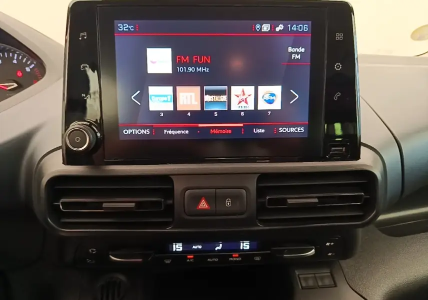 Écran tactile central allumé avec radio FM, tableau de bord noir du Peugeot Rifter blanc, vue intérieure frontale.
