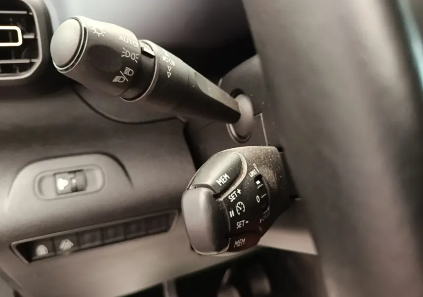 Gros plan sur les commandes au volant cuir du Peugeot Rifter blanc, avec réglages feux et régulateur de vitesse visibles.