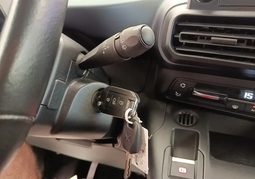 Gros plan intérieur sur le volant cuir et clé insérée dans le contacteur d’un Peugeot Rifter 2020, tableau de bord noir visible.