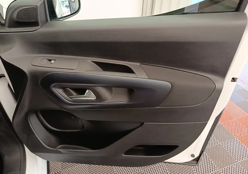 Vue rapprochée de la porte avant gauche noire du Peugeot Rifter blanc, montrant la poignée et les commandes de fenêtre.