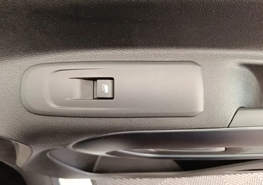 Gros plan sur le bouton de commande de la vitre électrique sur la porte intérieure noire d’un Peugeot Rifter blanc.