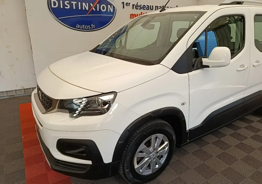 Vue 3/4 avant droit d'un Peugeot Rifter blanc avec phares LED et rétroviseurs blancs dans un showroom.