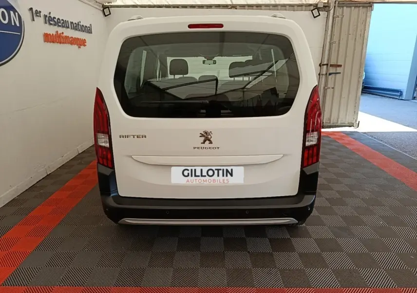 Vue arrière d'un Peugeot Rifter blanc 2020 avec feux arrière verticaux et pare-chocs noir dans un garage.