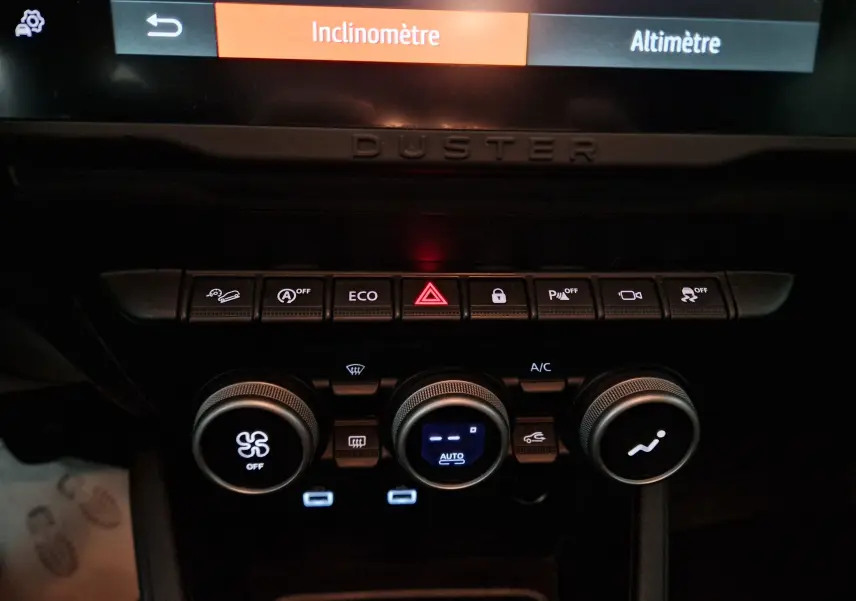 Détail du tableau de bord du Dacia Duster 2024 blanc montrant les commandes climatisation et boutons de fonctions assistées.