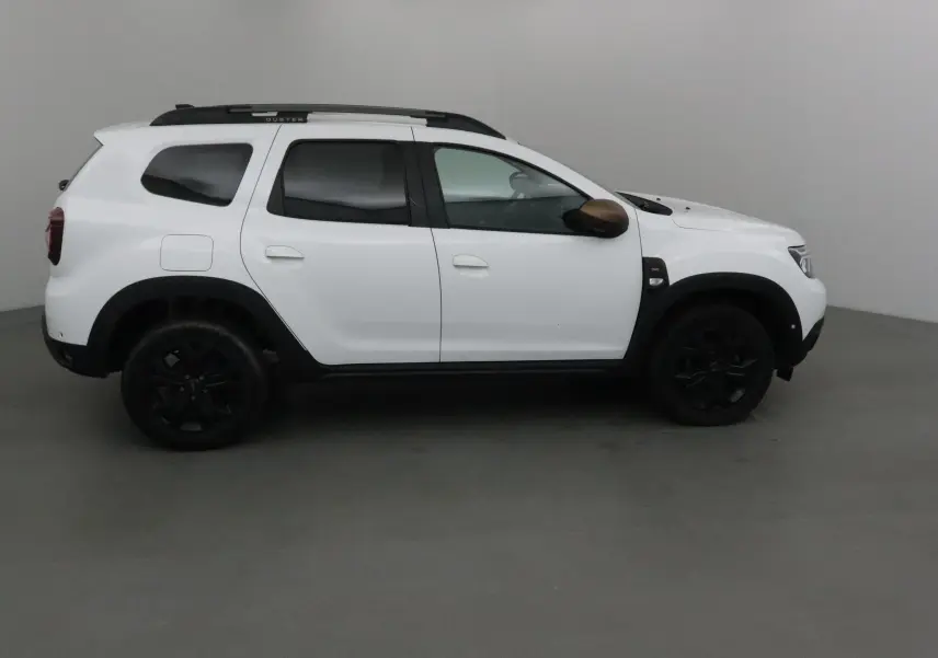 Profil côté droit d'un Dacia Duster 4x4 blanc 2024 avec jantes noires et coques de rétroviseurs marron.