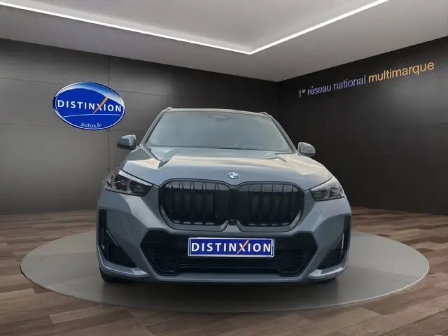 Vue frontale d'un BMW X1 Storm Bay avec calandre noire et projecteurs LED dans un showroom.