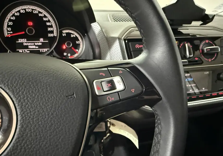 Gros plan sur le volant cuir et le tableau de bord du Volkswagen Up gris foncé, avec commandes multifonctions visibles.