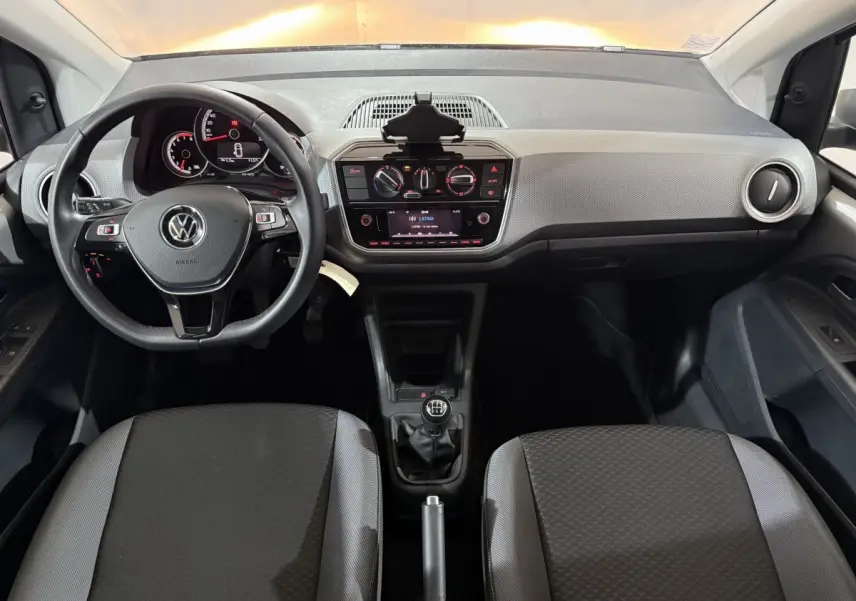 Vue intérieure avant du Volkswagen Up 1.0 65 Active avec tableau de bord clair, volant cuir et boîte manuelle.