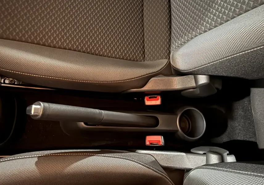 Vue rapprochée de la console centrale du Volkswagen Up gris foncé 2022, avec frein à main manuel et sièges en tissu.