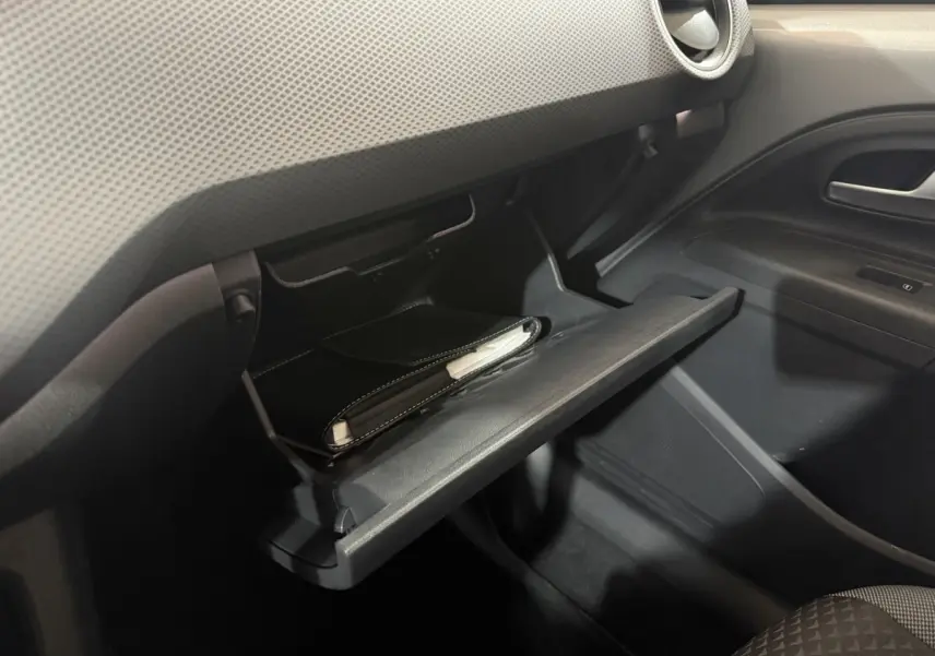 Gros plan sur la boîte à gants ouverte côté passager du Volkswagen Up gris foncé, avec un carnet à l'intérieur.