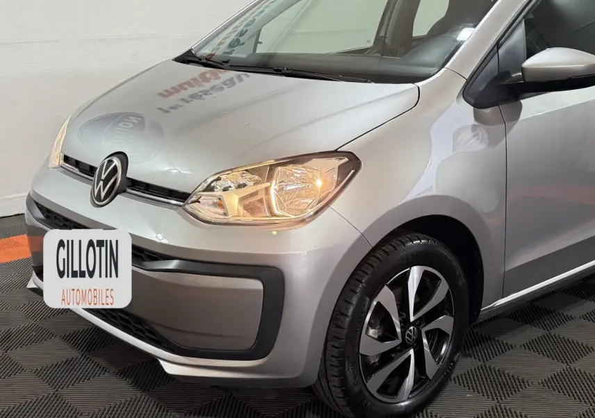 Vue 3/4 avant droit d'une Volkswagen Up gris foncé avec phares allumés et jantes alliage distinctives.
