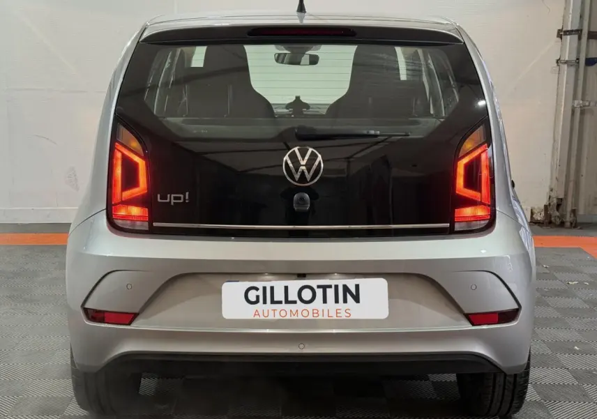 Vue arrière d'une Volkswagen Up! gris foncé avec feux arrière allumés et logo VW bien visible.