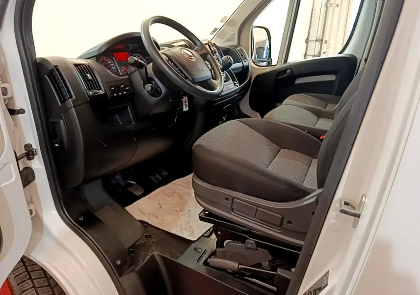 Vue intérieure côté conducteur du Fiat Ducato Fourgon blanc 2021, montrant le volant multifonctions et les sièges gris.