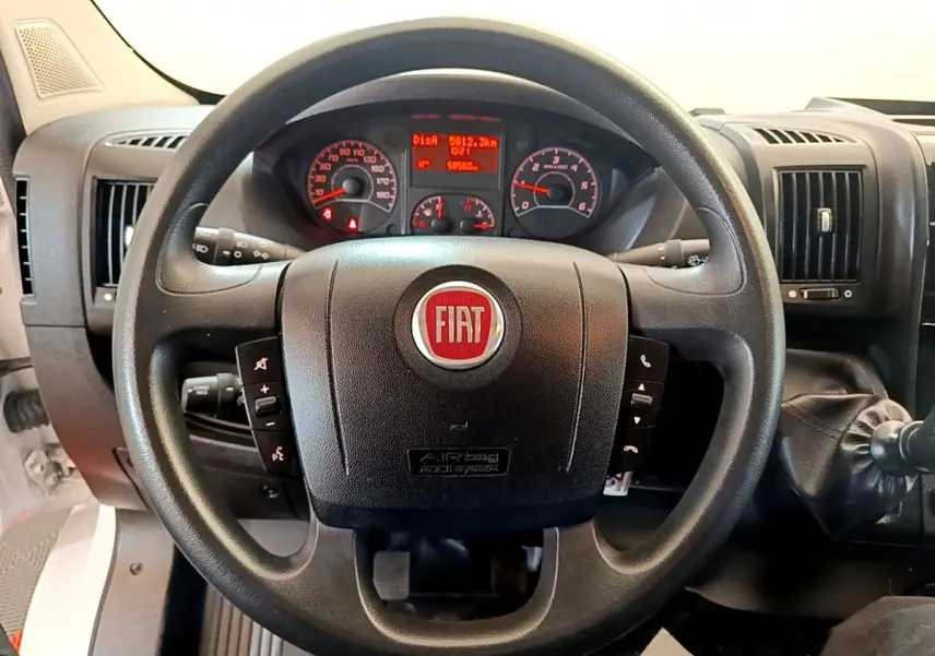 Vue rapprochée du volant noir multifonctions avec logo FIAT rouge et tableau de bord éclairé du Fiat Ducato Fourgon blanc.
