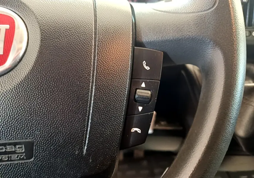 Gros plan sur le volant noir multifonctions du Fiat Ducato Fourgon blanc, mettant en valeur les commandes d’appel téléphonique.