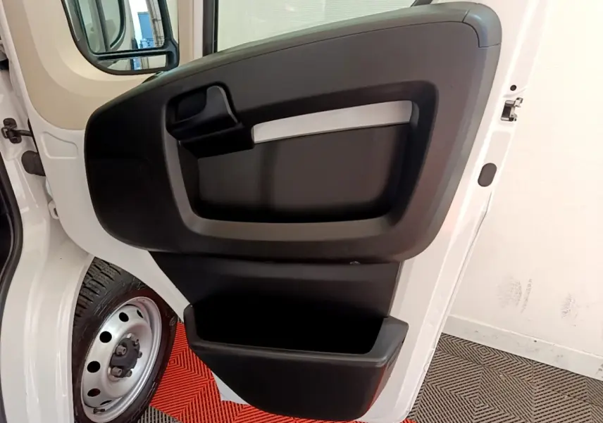 Vue rapprochée de la porte avant gauche ouverte d’un FIAT Ducato Fourgon blanc, avec rangement intégré noir.