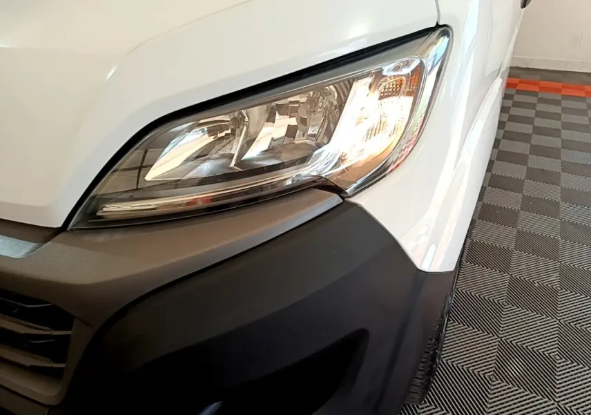 Gros plan sur le phare avant droit du FIAT Ducato Fourgon blanc, avec pare-chocs noir mat et partie de la calandre visible.