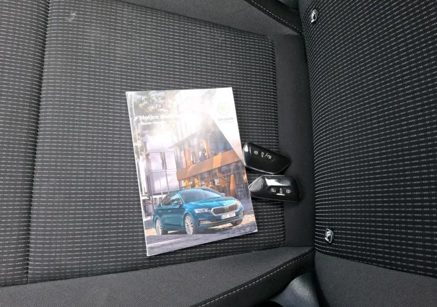 Notice d'utilisation SKODA Octavia posée sur un siège tissu noir à rayures fines avec deux clés de voiture noires.
