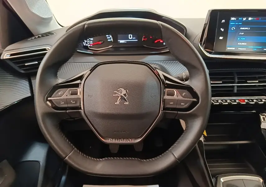 Vue intérieure centrée sur le volant cuir multifonctions de la Peugeot 208 2023 avec tableau de bord numérique et écran tactile.