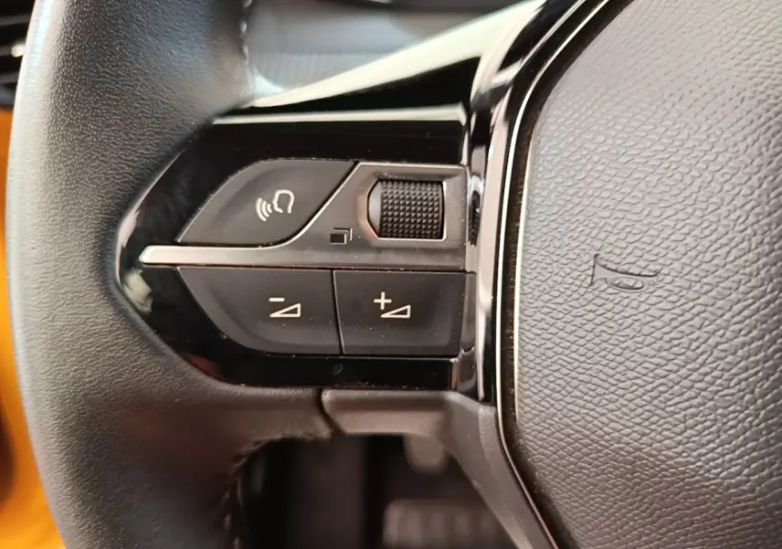 Gros plan sur le volant cuir noir multifonctions de la Peugeot 208 jaune, avec commandes audio intégrées.