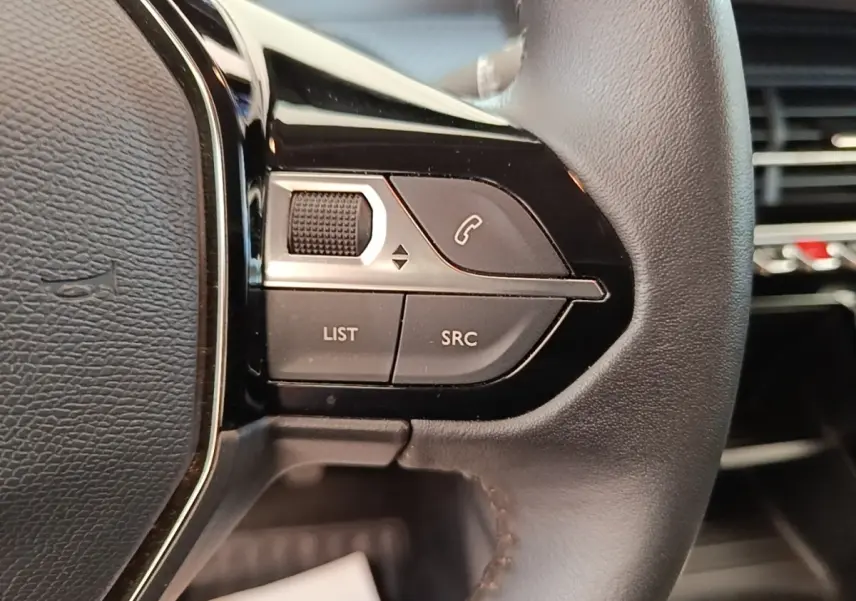 Gros plan sur les commandes gauche du volant cuir noir de la Peugeot 208 jaune, avec boutons multifonctions et molette.