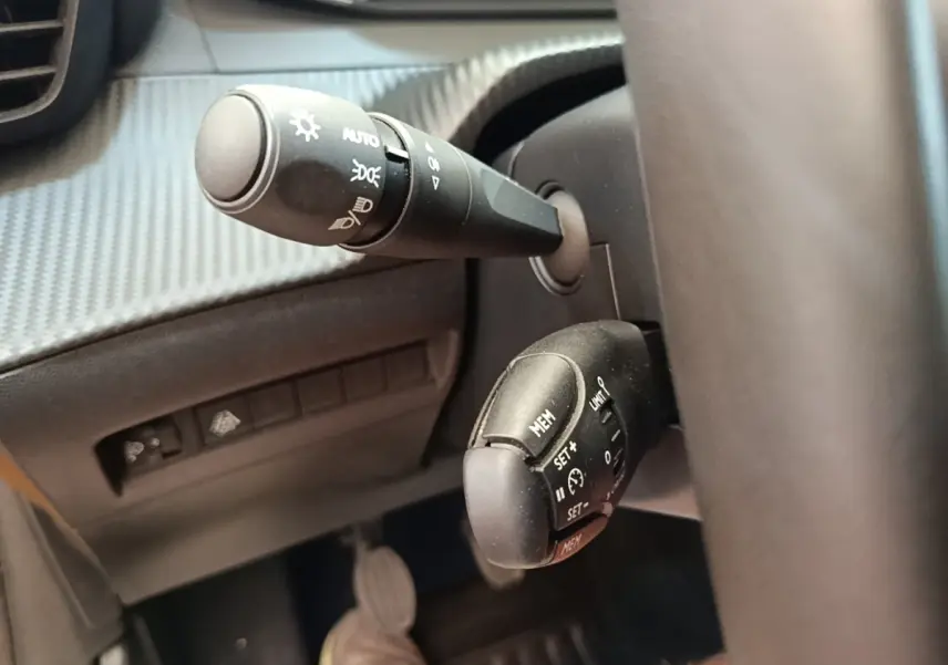 Gros plan sur la commande de régulateur de vitesse et les commandes d’éclairage du Peugeot 208 PureTech jaune, côté conducteur.