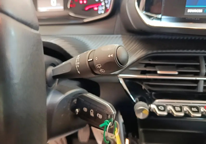 Gros plan sur la colonne de direction et le volant cuir de la Peugeot 208, avec tableau de bord et commandes visibles.