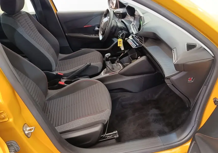 Intérieur avant droit d'une Peugeot 208 jaune 2023, volant cuir multifonctions et tableau de bord avec écran tactile.