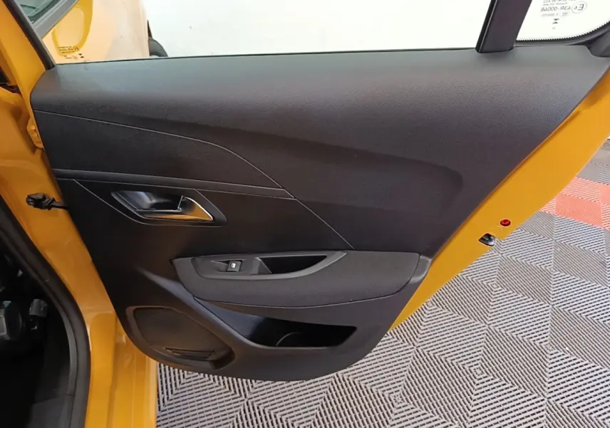 Vue rapprochée de la porte avant gauche noire d’une Peugeot 208 jaune 2023, avec poignée et commande de vitre.