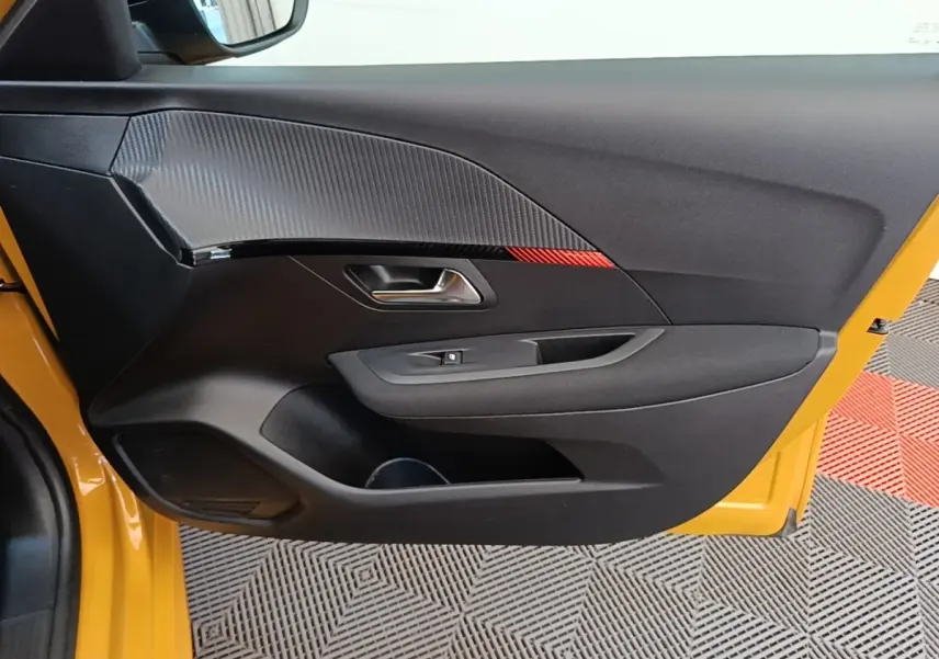 Vue latérale de la porte avant gauche noire avec insert effet carbone et bande rouge sur Peugeot 208 jaune 2023.
