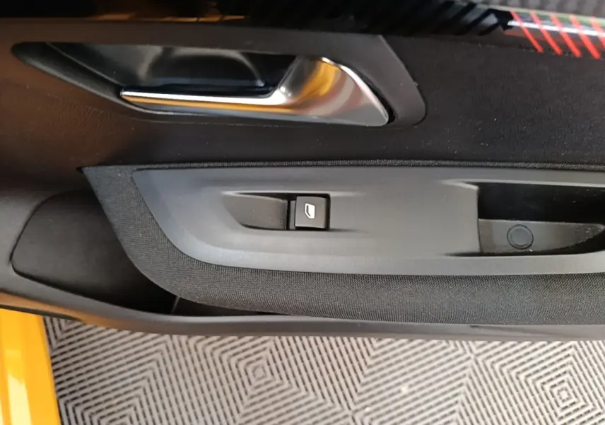 Détail de la porte côté conducteur d’une Peugeot 208 jaune 2023, avec poignée argentée et bouton de lève-vitre.