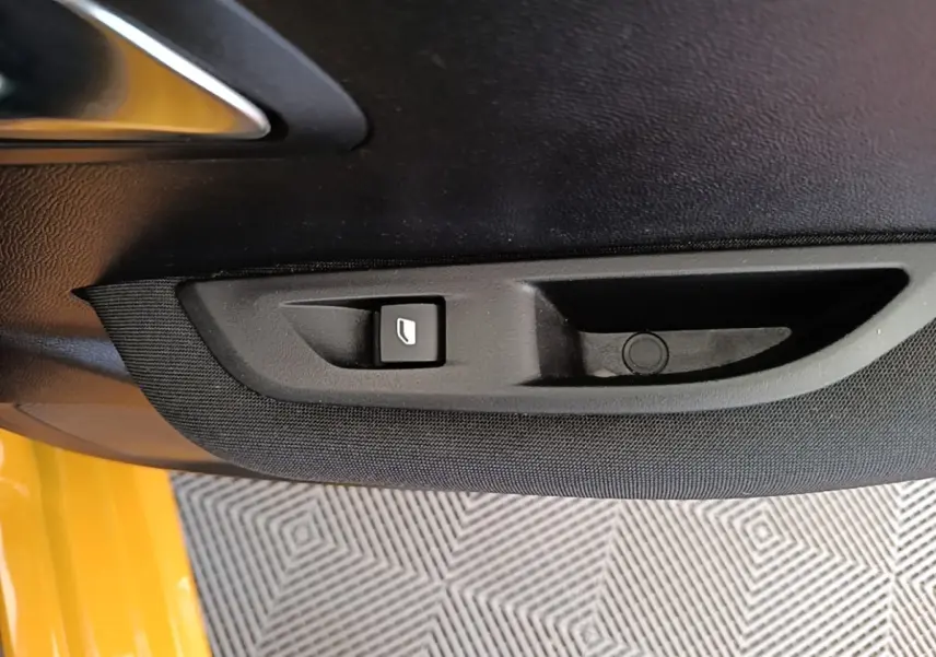 Détail de la commande de lève-vitre électrique sur la porte intérieure côté conducteur d'une Peugeot 208 jaune.
