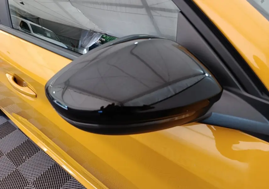 Rétroviseur extérieur noir côté gauche d'une Peugeot 208 jaune vue en gros plan sur fond intérieur.