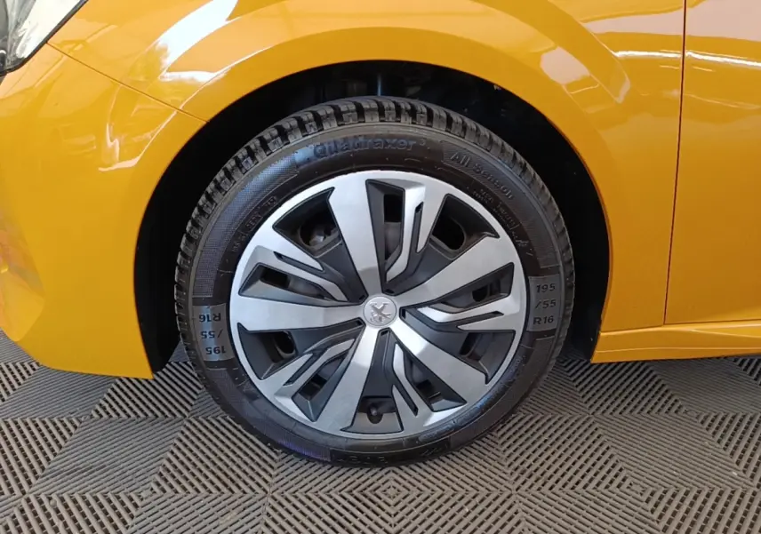 Gros plan sur la roue avant gauche d’une Peugeot 208 jaune 2023 avec jante en alliage au design moderne.