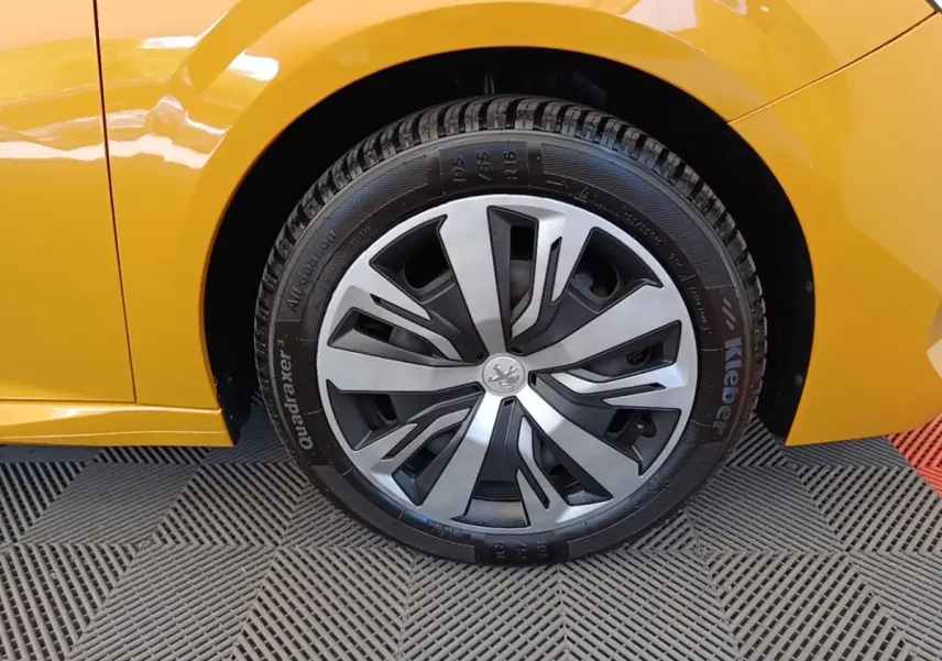 Gros plan sur la roue avant droite de la Peugeot 208 jaune 2023 avec jante alliage au design moderne.