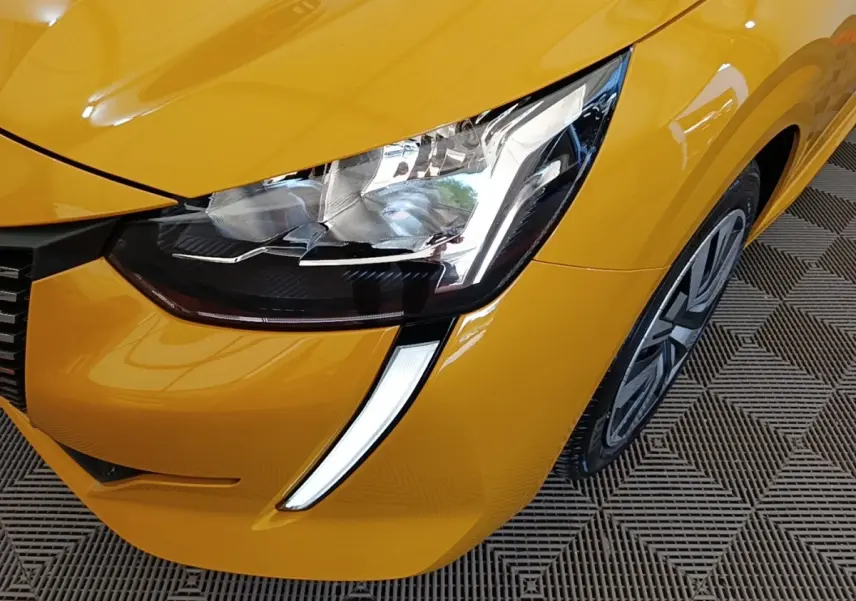 Gros plan sur le phare avant gauche et la roue d’une Peugeot 208 jaune PureTech 75 S&S Active Pack 2023.