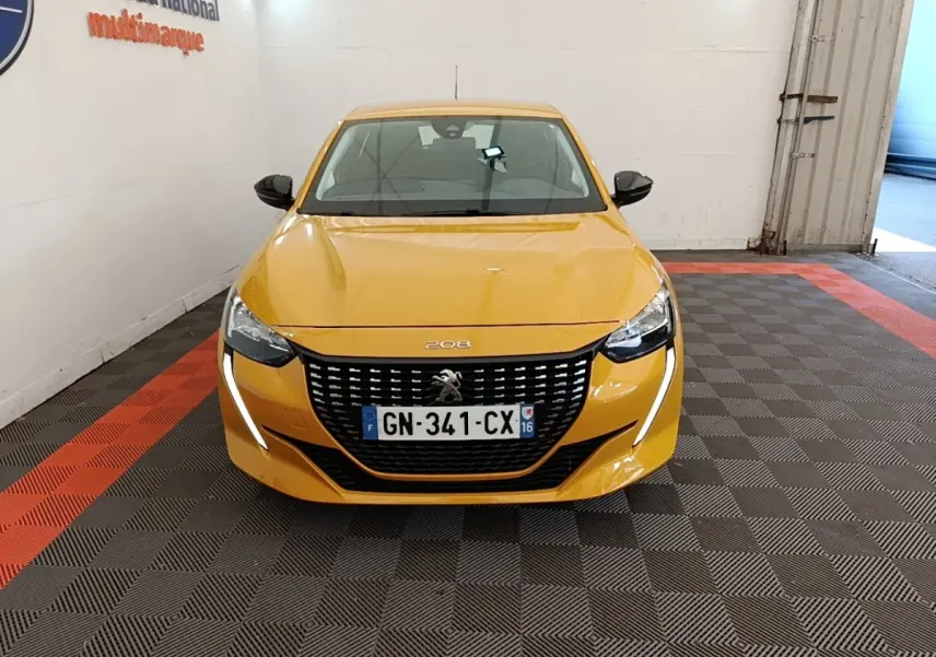 Peugeot 208 jaune vue de face en intérieur, avec calandre noire et feux LED en forme de griffes.