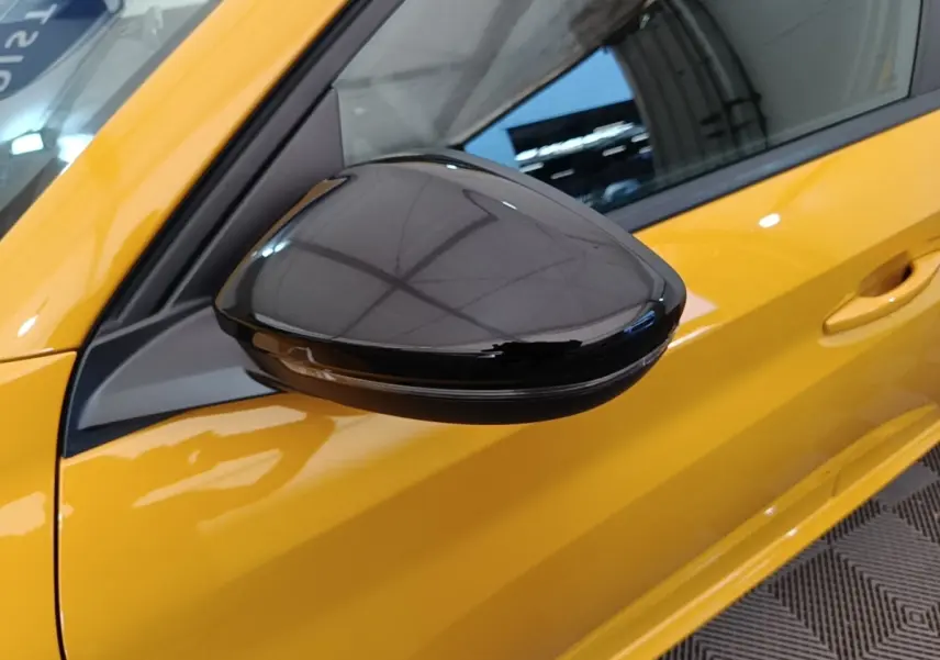 Gros plan sur le rétroviseur noir brillant côté gauche d’une Peugeot 208 jaune vif, vue latérale avant.
