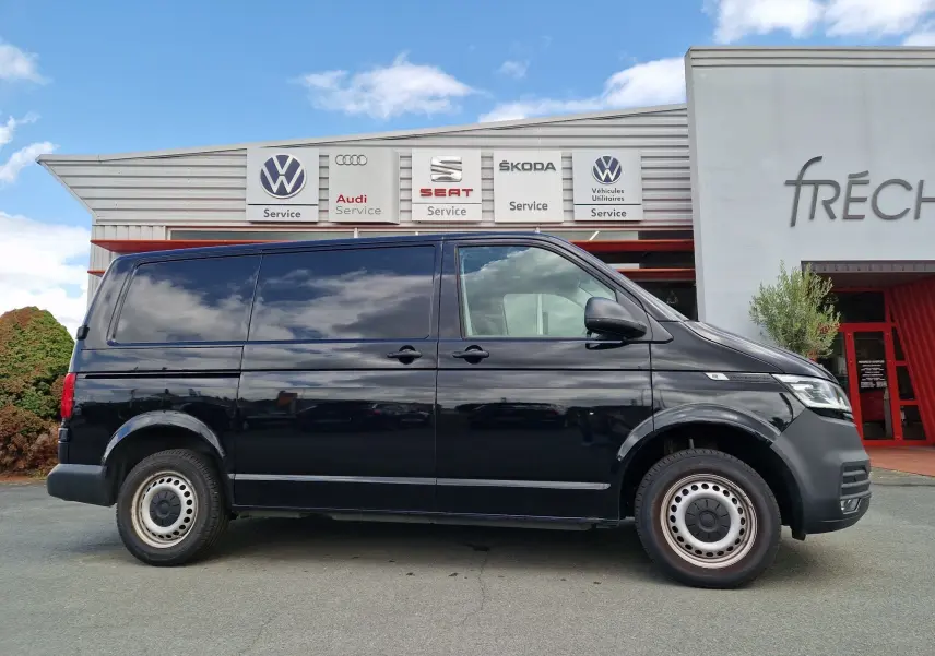Profil côté droit d'un Volkswagen Transporter noir 2020 garé devant un centre de service multimarques.