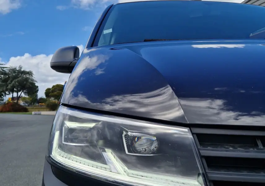 Gros plan sur l'avant droit du Volkswagen Transporter noir 2020, mettant en valeur son projecteur LED et la calandre.