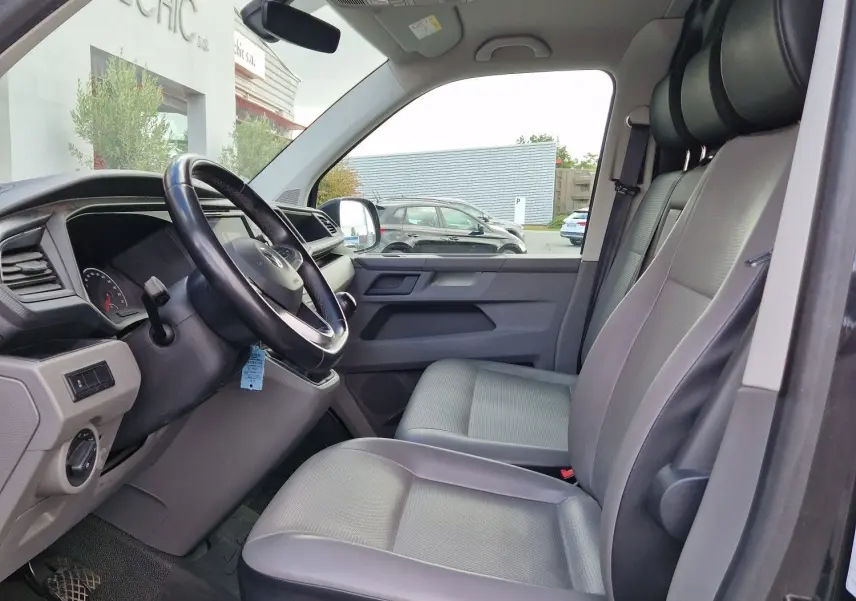 Vue intérieure côté conducteur du Volkswagen Transporter noir 2020, montrant le volant multifonction et les sièges avant gris.